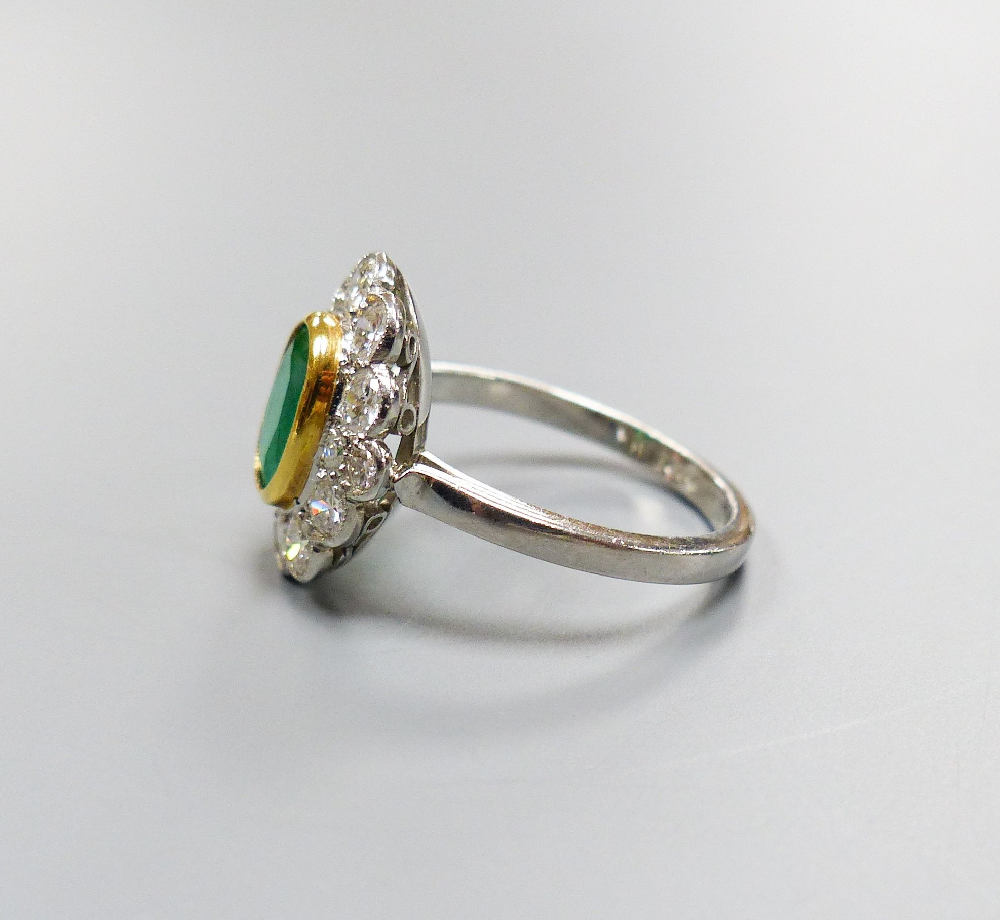 A modern platinum, emerald and diamond set oval cluster ring, size M, gross weight 5.2 grams.